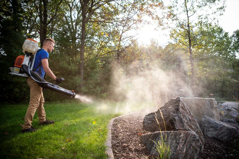 A man mows grass with a gas-powered mower, implementing mosquito control measures in Los Angeles, CA.